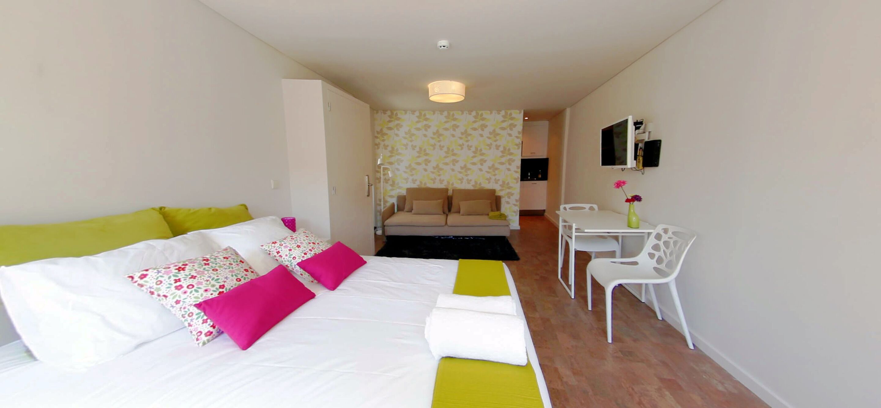 A bedroom with a bed, a desk, and a chair. There is a sofa in the background.