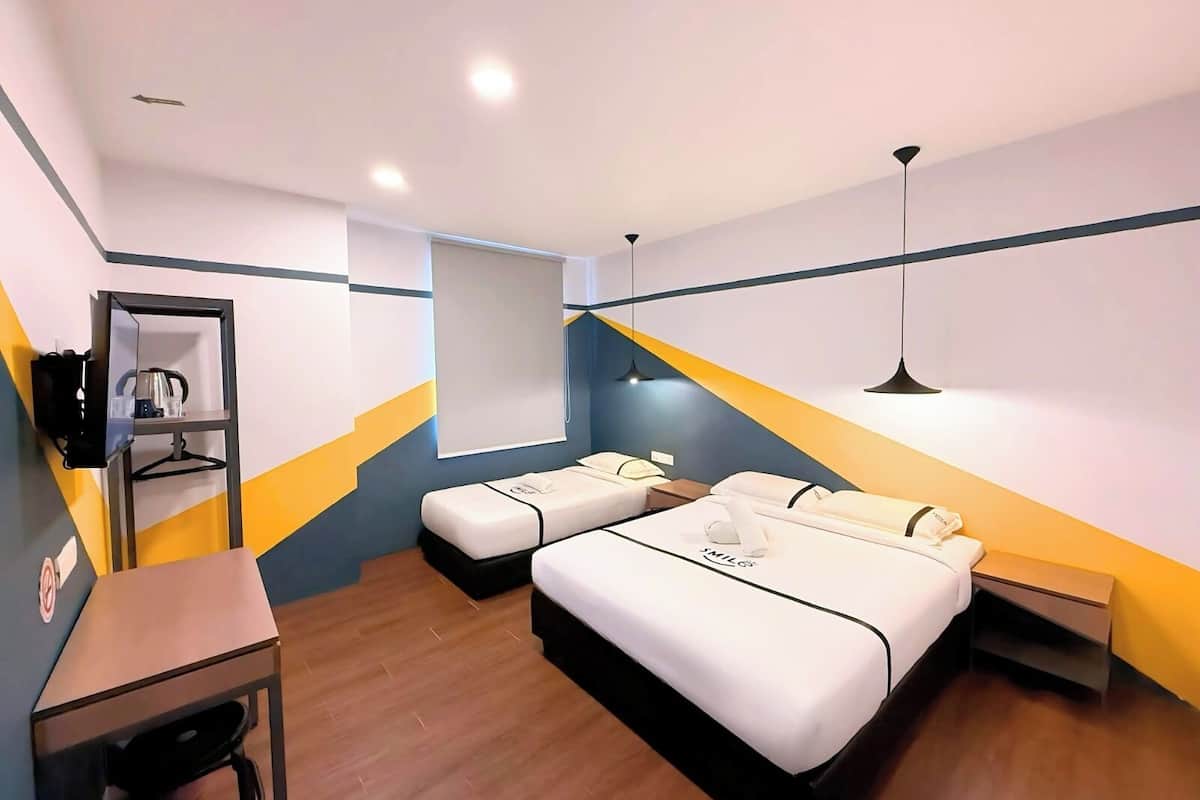 Habitación de hotel con dos camas, un escritorio, una silla, un armario y un espejo.