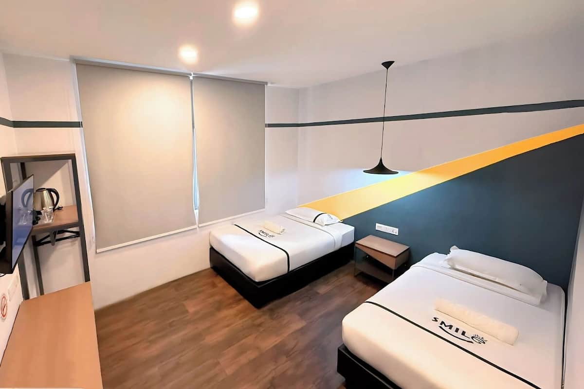 Una habitación de hotel con dos camas, un escritorio, una silla, una lámpara y una ventana.