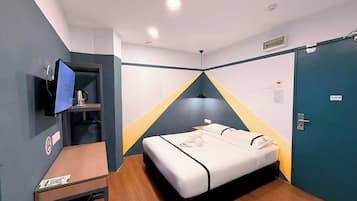 A hotel room with a bed, a desk, a TV, and a door.