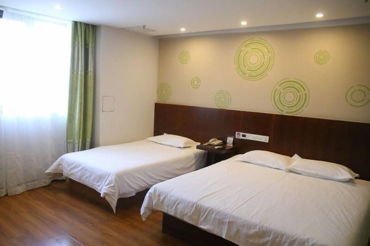 A hotel room with two single beds, wooden flooring, a green curtain, and a wall with circular patterns.