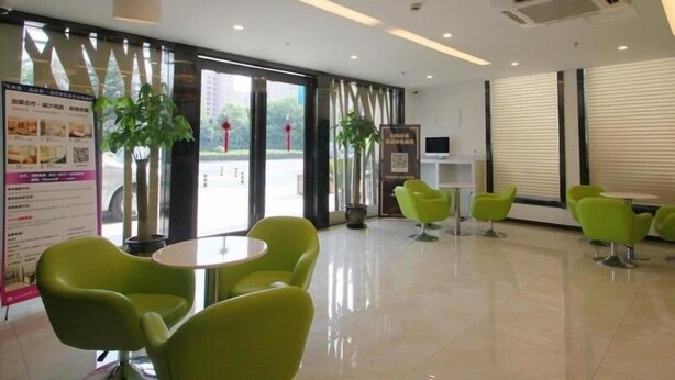 A modern lobby with green chairs, a reception desk, and a large window with blinds. - GreenTree Inn Shanghai Hotel (Shanghai)