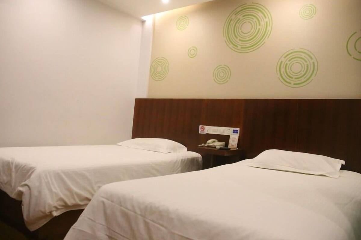 A hotel room with two single beds, a wooden headboard, and a wall with circular patterns.