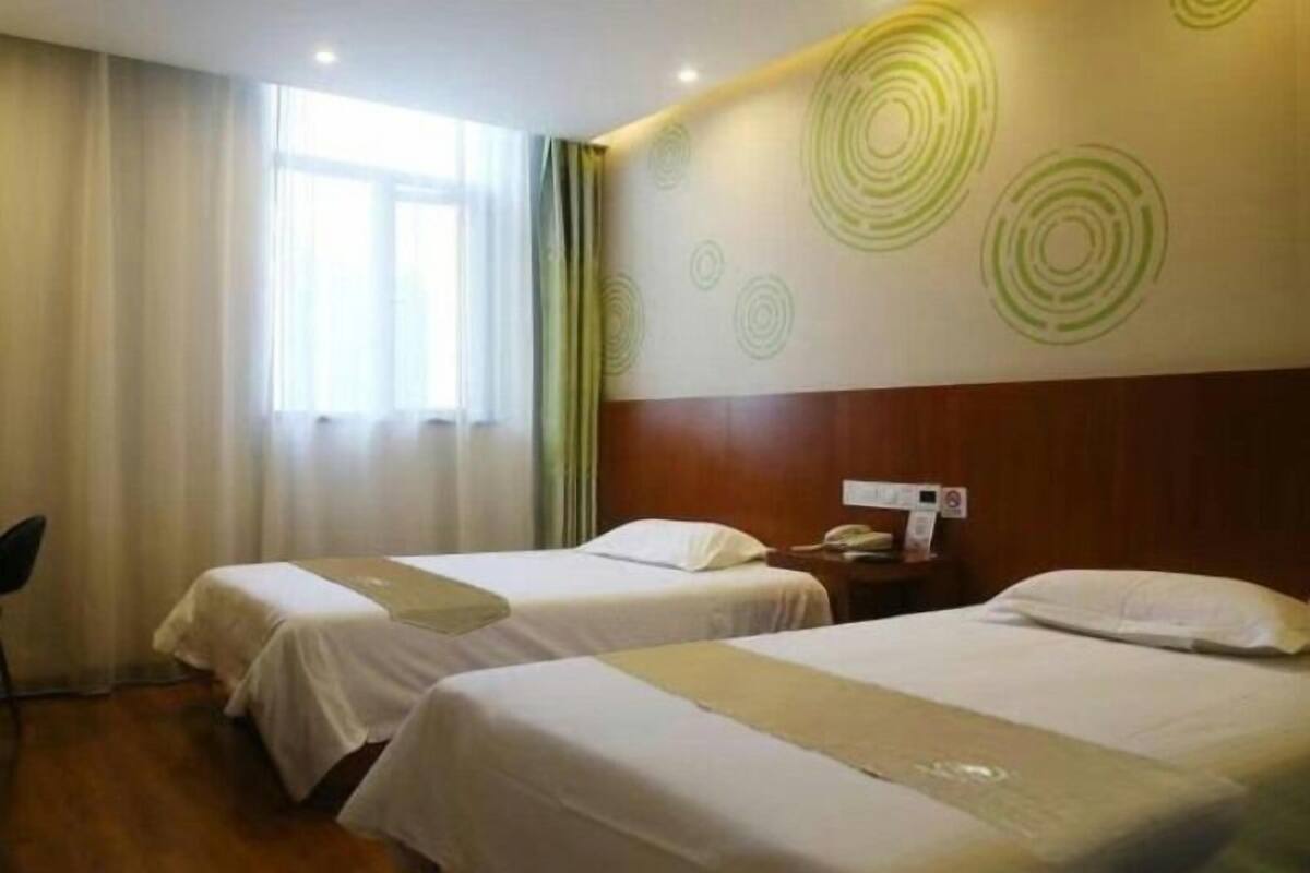 A hotel room with two beds, a wooden headboard, a nightstand with a phone, and a window with curtains.