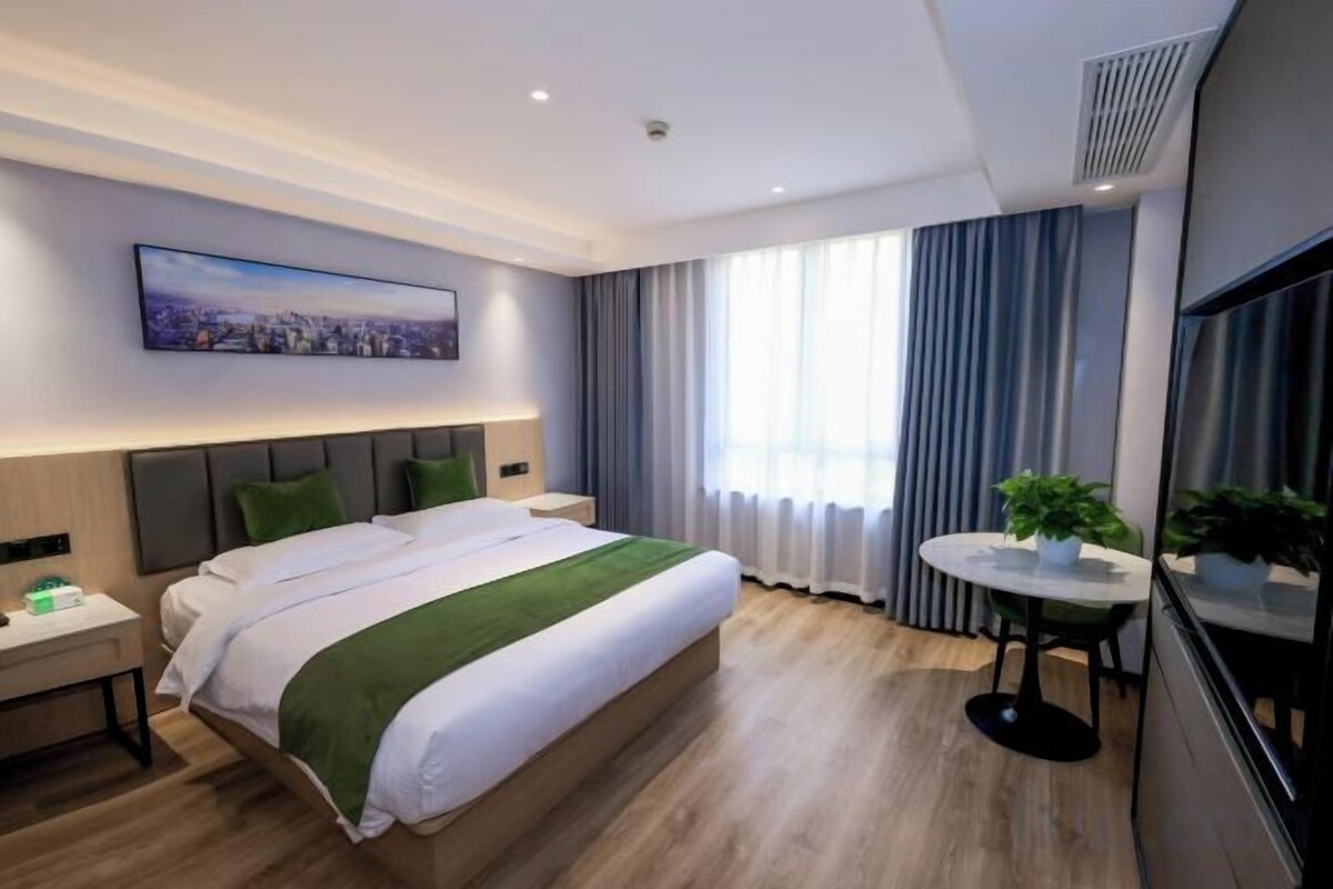A hotel room with a large bed, a bedside table, a round table with a plant, and a television.