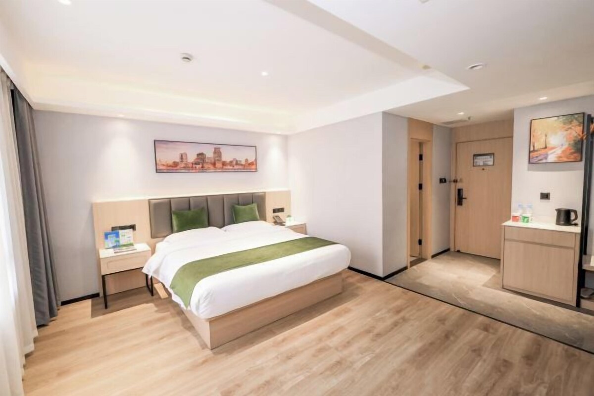 A modern hotel room with a large bed, a bedside table, a nightstand, a wardrobe, and a small kitchenette.