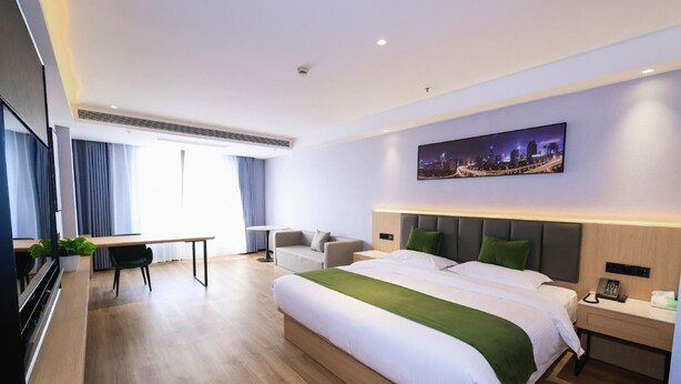 Et moderne hotelværelse med en stor seng, et skrivebord, en stol, en sofa og et bybillede på væggen.