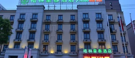 A hotel with a green signboard and a red signboard. There are two cars parked in front.