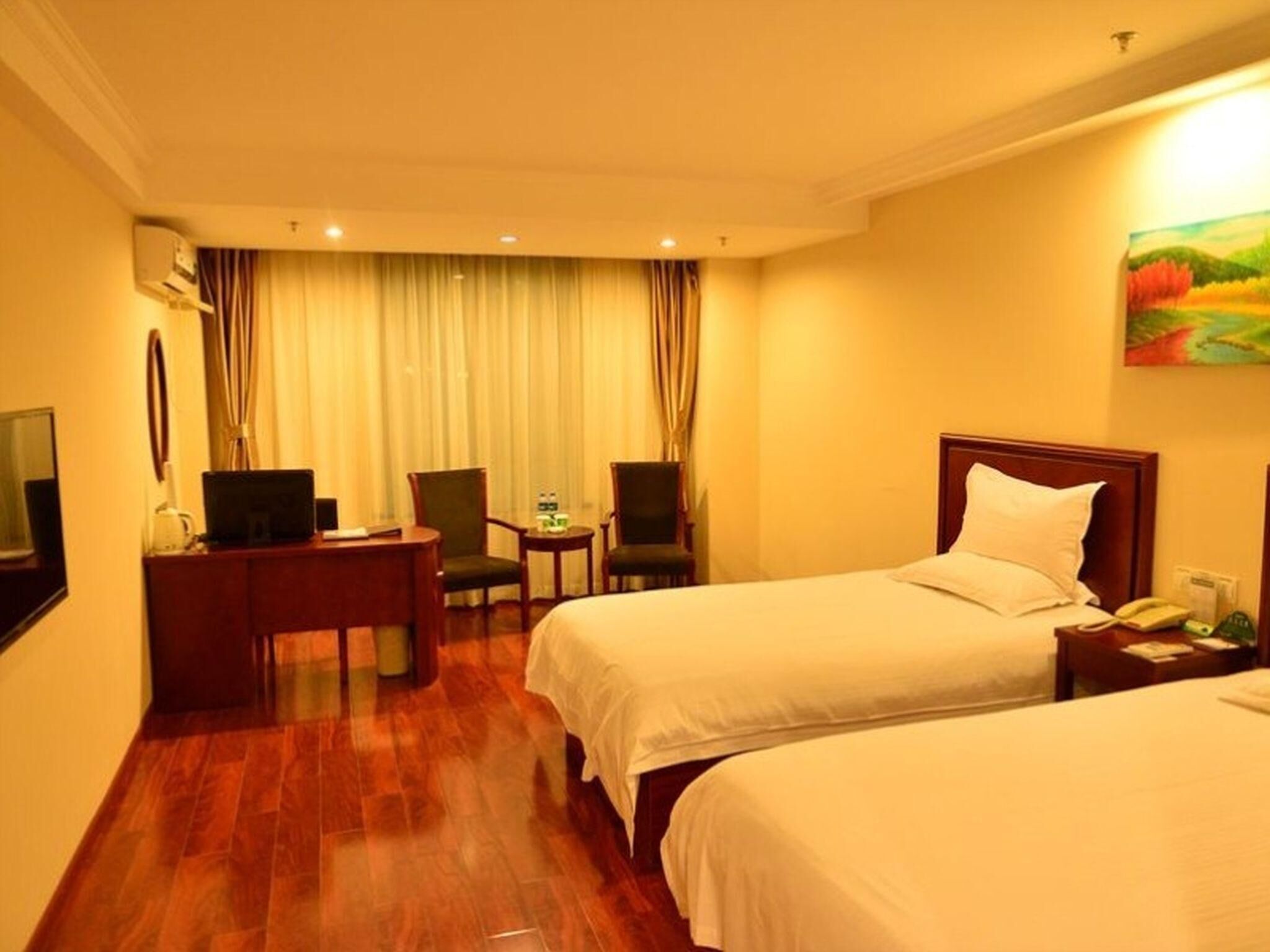 A hotel room with two beds, a desk with a computer, a chair, a small table with a water bottle, and a painting on the wall.