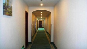 En hotelgang med tæppedejlig gulv, hvide vægge og en løber i grønt.