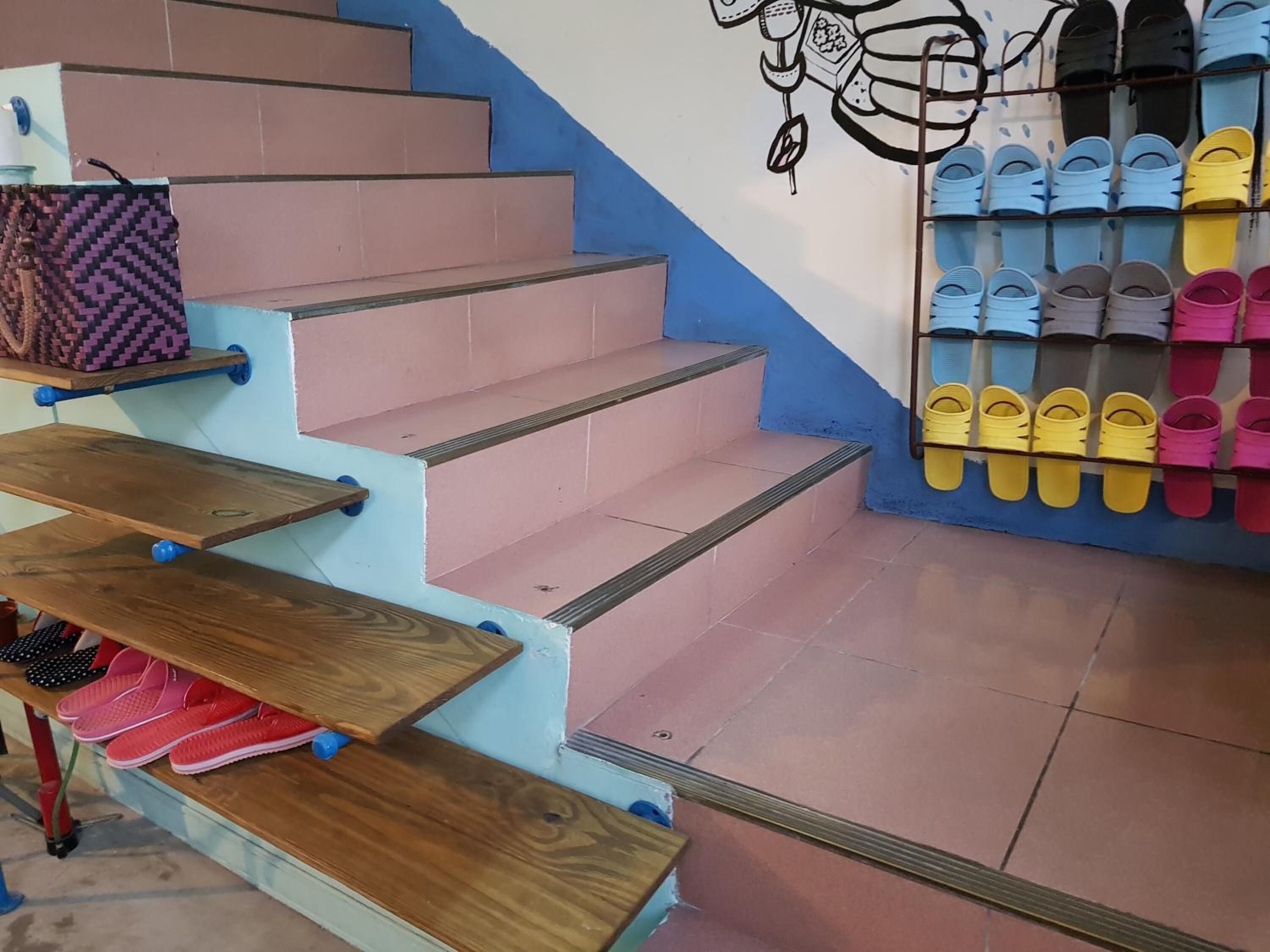 A staircase with pink steps, wooden handrails, and a wall-mounted shoe rack with various slippers.