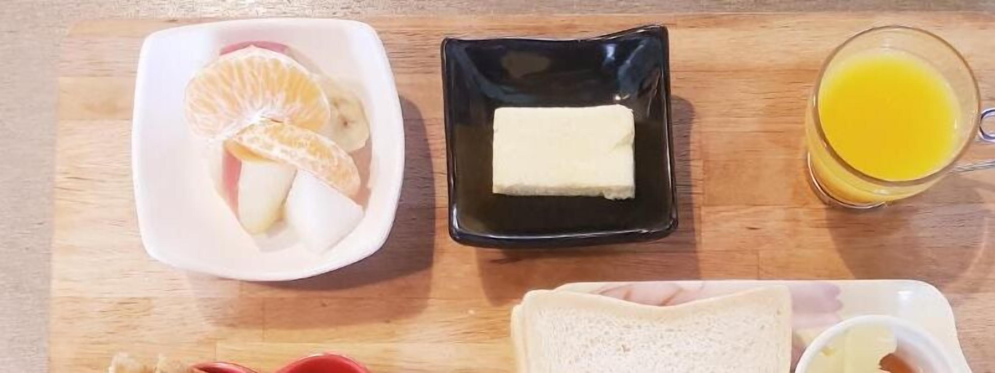 A breakfast tray with orange slices, butter, toast, and orange juice on a wooden table.