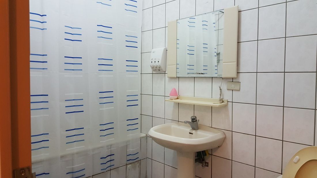 A bathroom with white tiled walls, a white sink, a mirror, and a toilet.