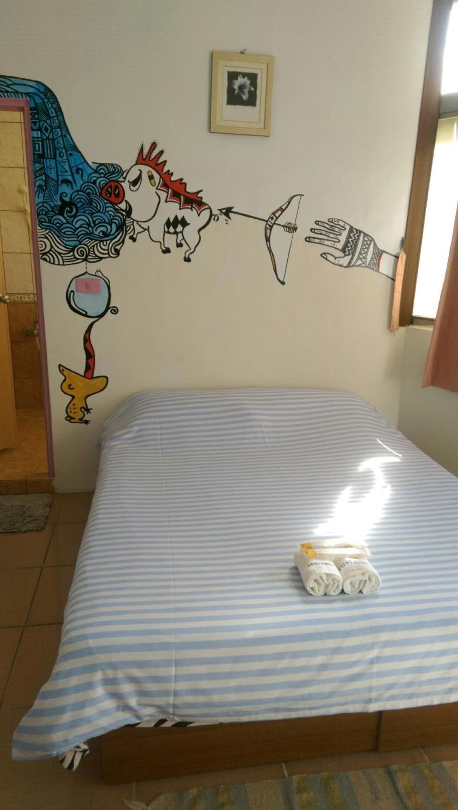 Habitació amb un llit, un mural a la paret i una finestra.