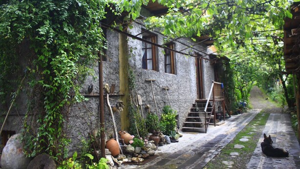 Un étroit sentier de pierres mène à un bâtiment rustique doté d’un escalier en bois.