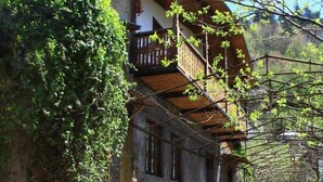 Un bâtiment rustique en pierre, doté d’un balcon en bois, entouré de verdure et de vélos.