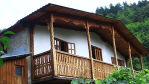 Une maison traditionnelle en bois, dotée d’un balcon et entourée de verdure.