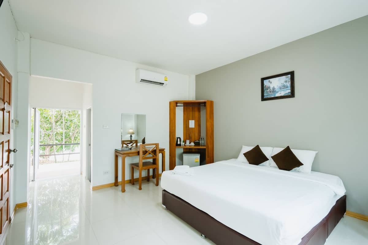Habitación de hotel con cama, escritorio, silla, refrigerador pequeño y ventana con vista a zonas verdes.