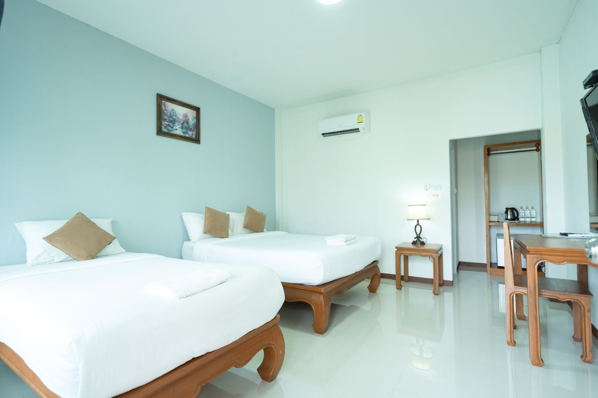 A hotel room with two beds, a desk, a chair, a lamp, an air conditioning unit, and a framed picture on the wall.