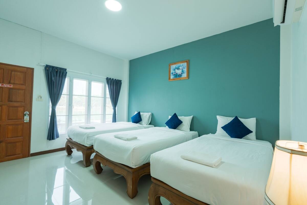 Habitación de hotel con dos camas, una puerta de madera, una ventana con cortinas y un cuadro colgado en la pared.