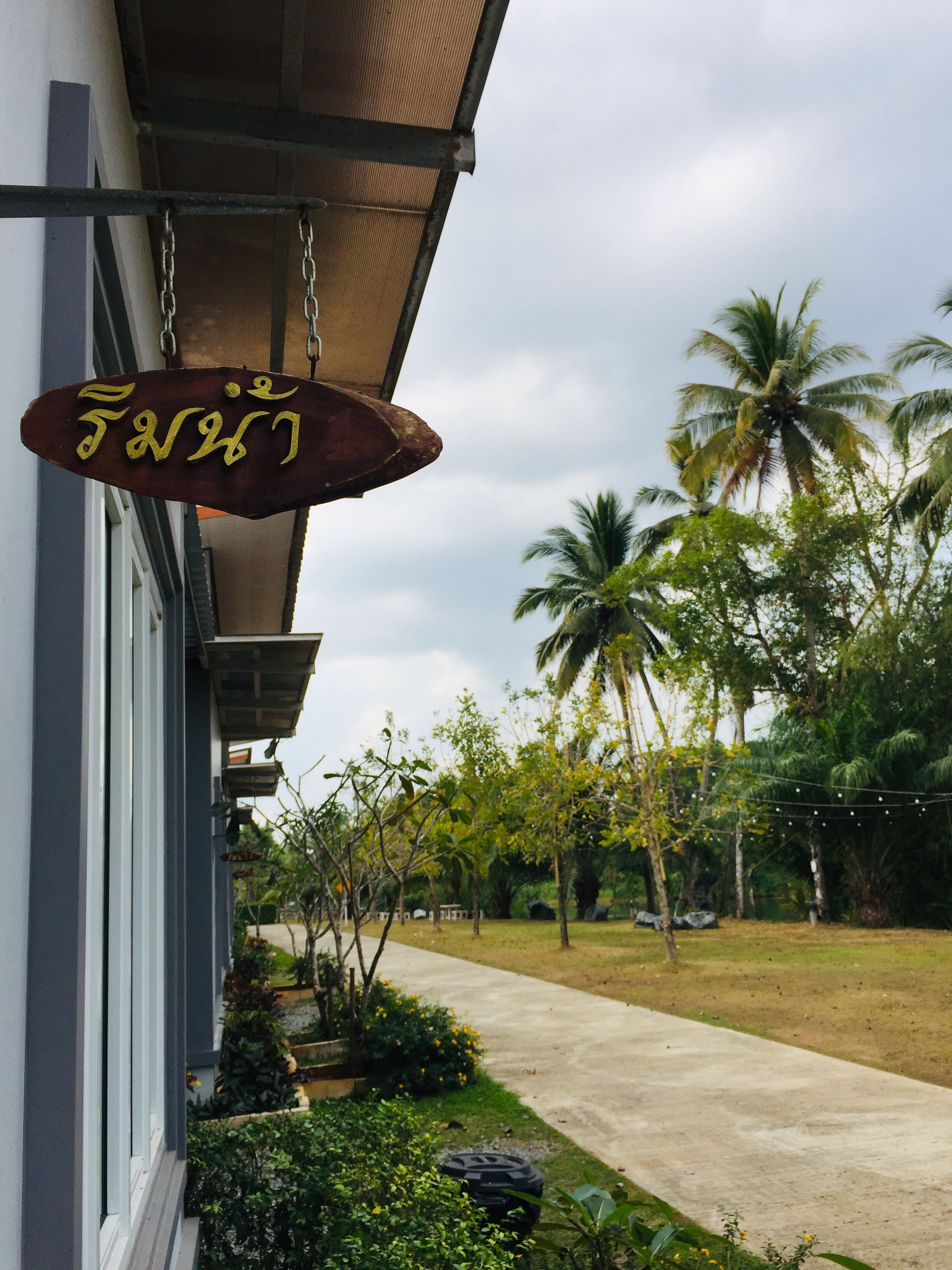 A building with a hanging sign, a pathway, and palm trees in the background.