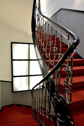 Una escalera con barandillas de metal decoradas y peldaños alfombrados de rojo.