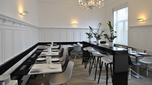 Een moderne keuken met een lange eettafel, barkrukken en hanglampen.