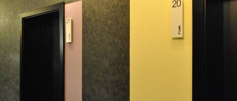 A hallway with numbered doors, light fixtures, and a textured wall.