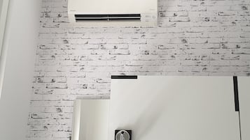 Una habitación con pared de ladrillo blanco, unidad de aire acondicionado blanca, una puerta con manija y una lámpara.
