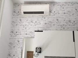 Una stanza con una parete in mattoni bianchi, un condizionatore bianco, una porta con maniglia e un lampadario.