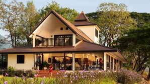 A two-story house with a balcony, a covered porch, and a garden with purple flowers. - Wopakok Hotel (Pakse)