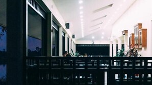 A corridor with a railing, leading to a brightly lit room with a ceiling fan and a view of the outside. - Wopakok Hotel (Pakse)