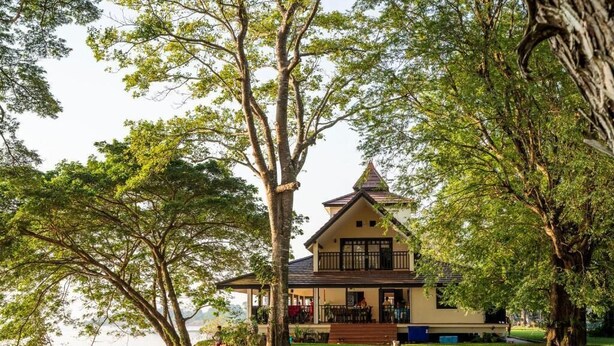 A two-story house with a balcony, surrounded by trees and a stone wall. - Wopakok Hotel (Pakse)