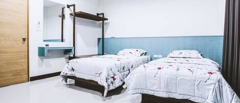 Een slaapkamer met twee bedden, een houten deur, een spiegel en een blauwe accentmuur.