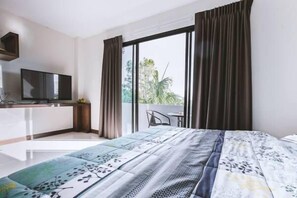 A modern hotel room with a large bed, a flat-screen TV, a small desk, and a balcony with a view of greenery. - Ra Residence Phuket (Chalong)