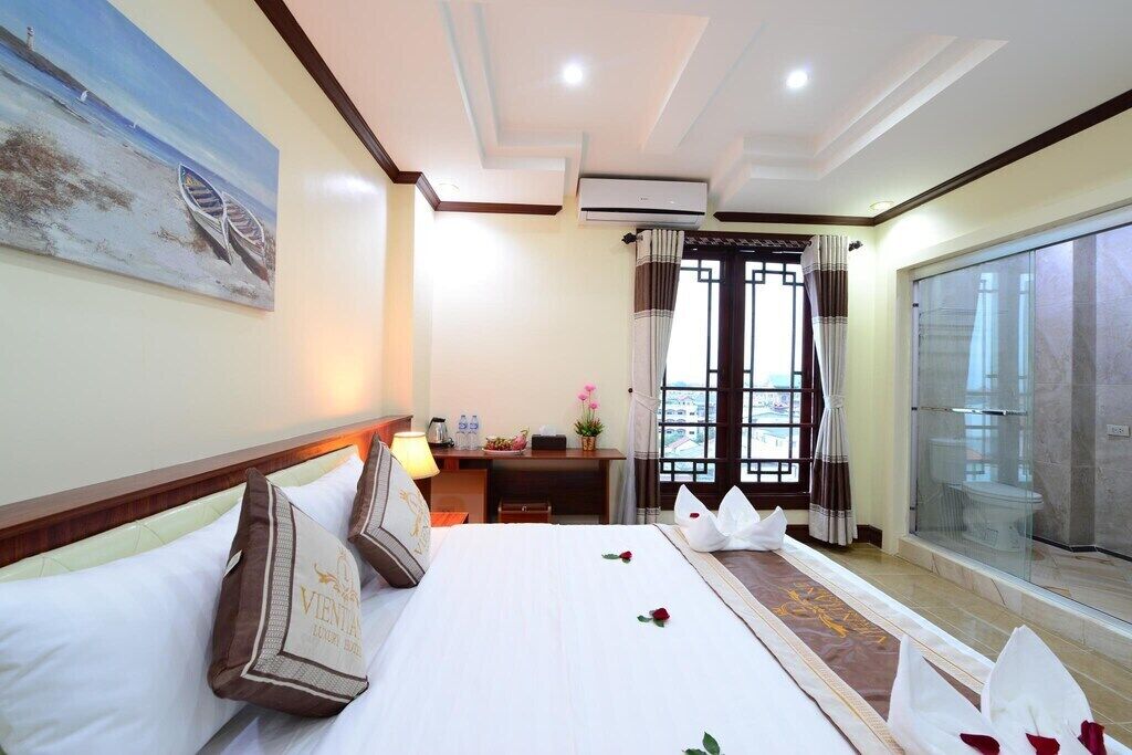 Habitación de hotel con cama, escritorio, silla, ventana con cortinas y un cuadro en la pared.
