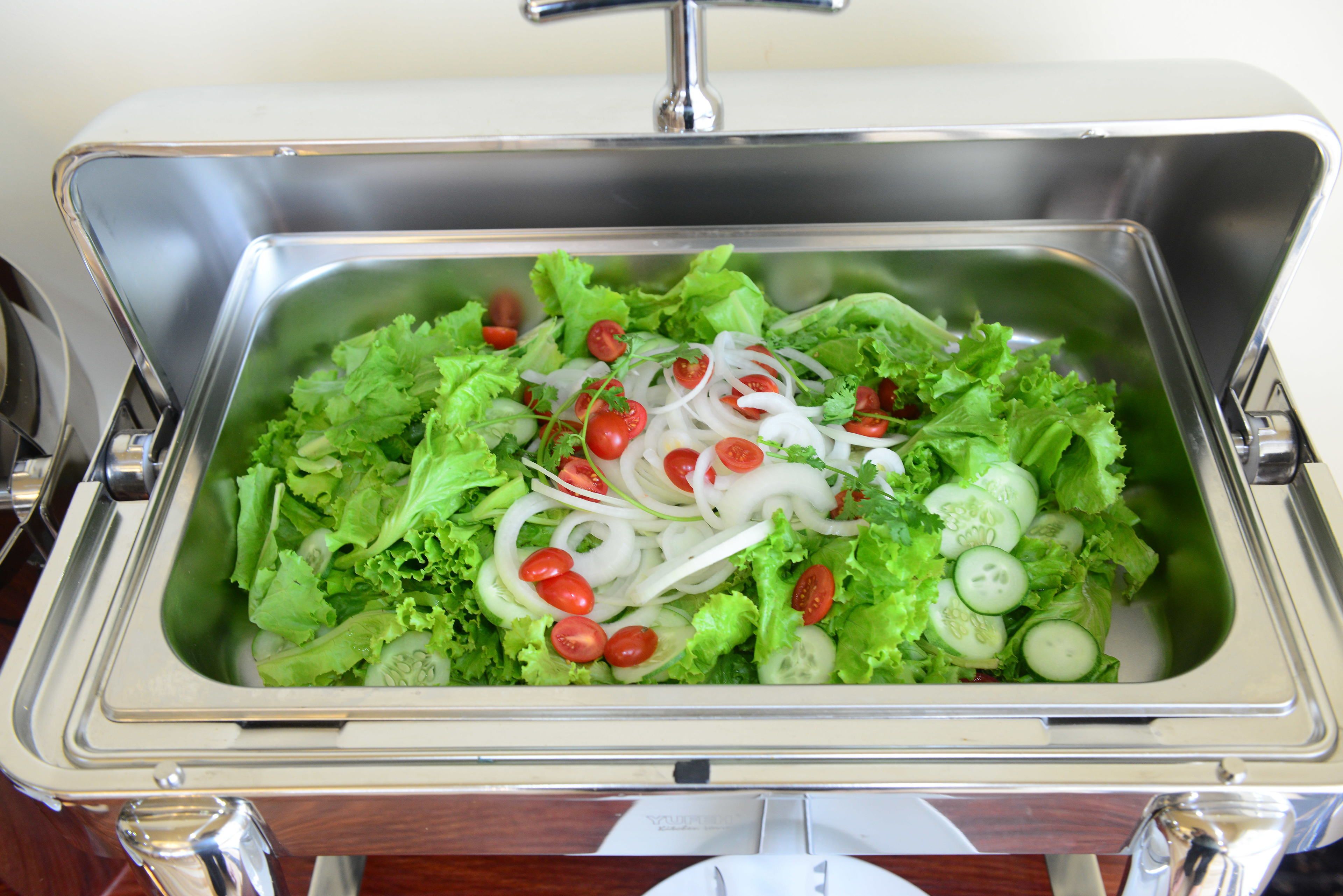 A stainless steel sink with a salad containing lettuce, tomatoes, cucumbers, and onions.