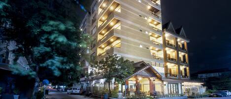 Un hotel de varios pisos con un letrero llamativo que dice "VIENTIANE LUXURY HOTEL" en la parte superior. El edificio cuenta con balcones en cada piso, una entrada cubierta y está rodeado de árboles y coches estacionados.