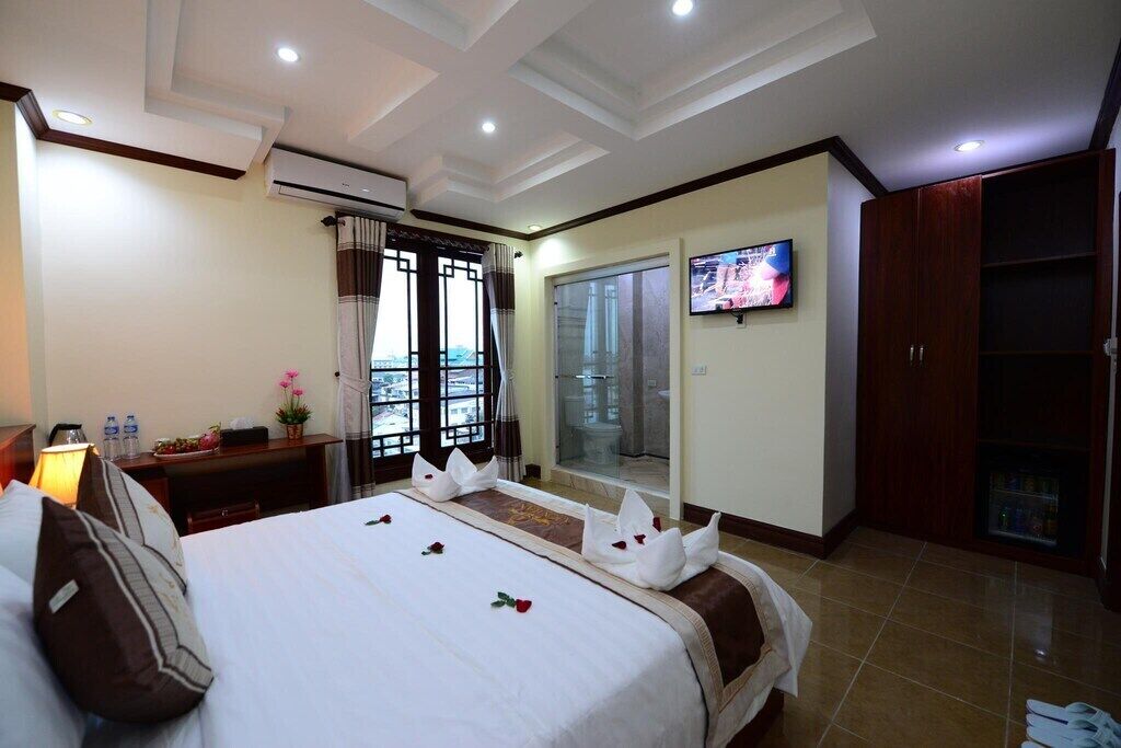 A hotel room with a neatly made bed, a television on the wall, a wardrobe, and a balcony with a view.