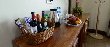 Una mesa de madera con una cesta de mimbre que contiene botellas, una cafetera y un bol de fruta.