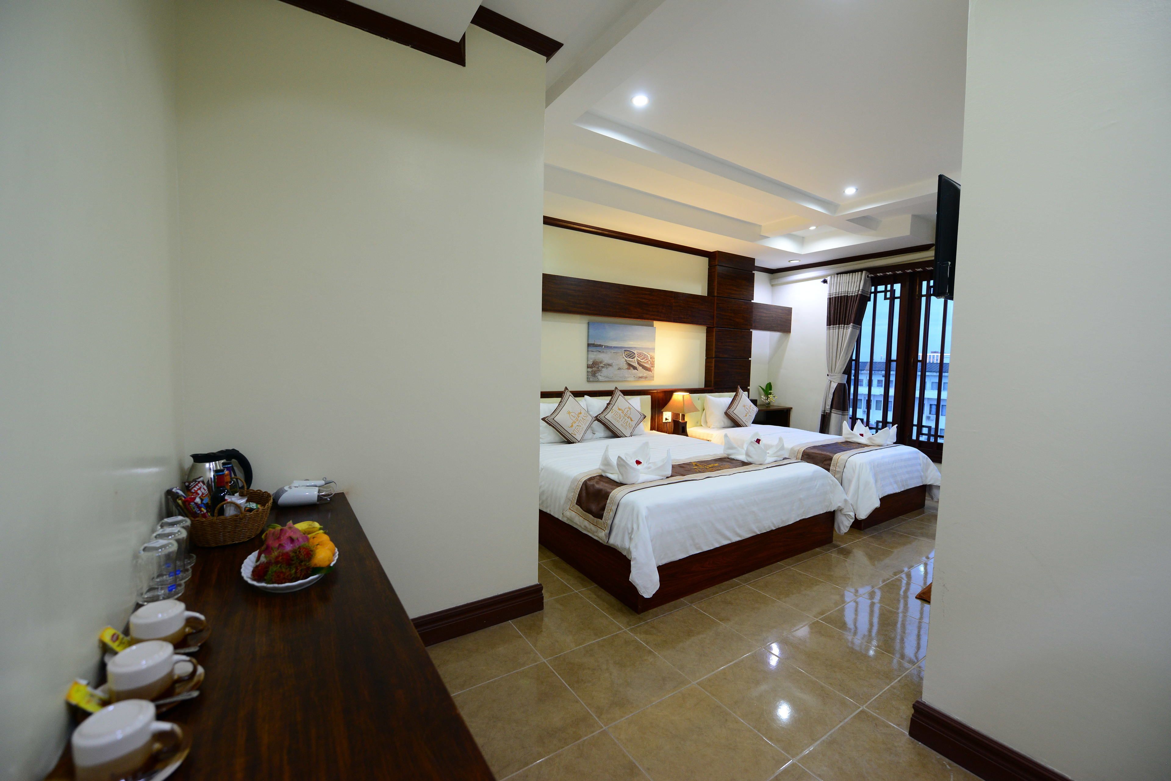 A hotel room with two beds, a dining table with breakfast items, and a view of the outdoors.