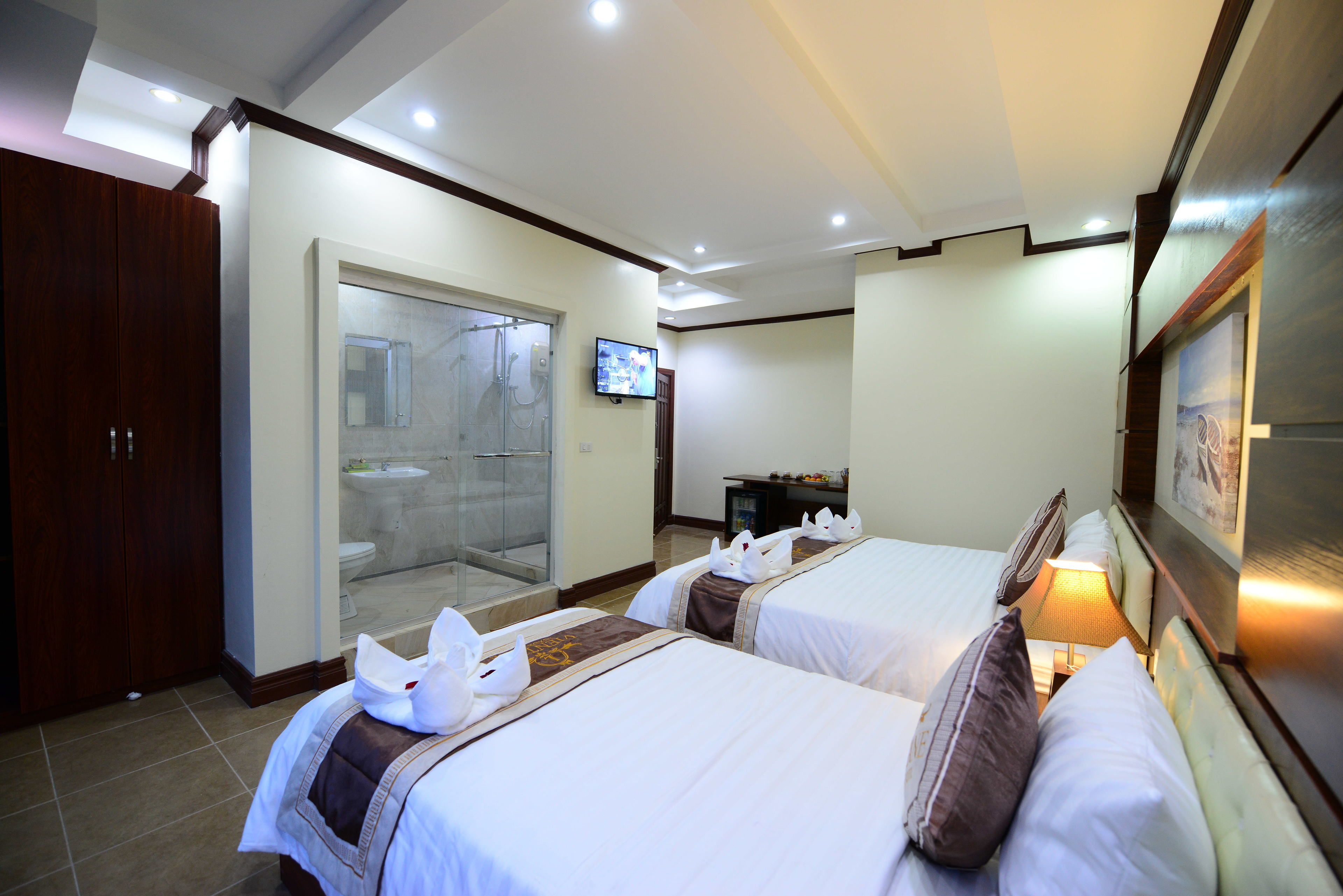 Quarto de hotel com duas camas, televisão, chuveiro e escrivaninha.