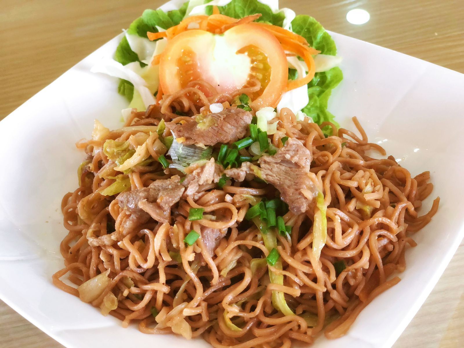 A bowl of noodles with beef and vegetables, served with a side salad.
