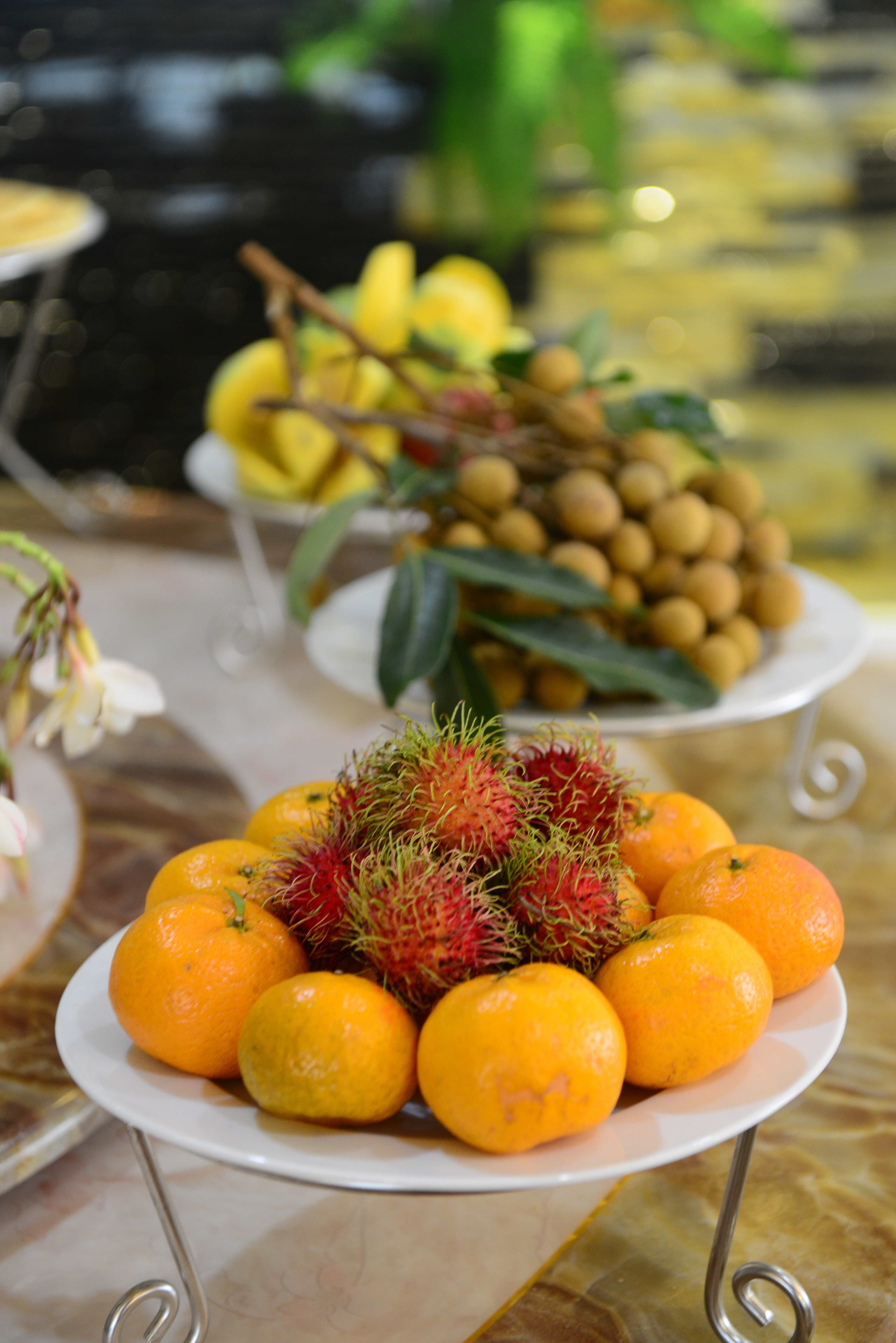 Una mesa con platos de frutas, incluyendo naranjas y rambután.
