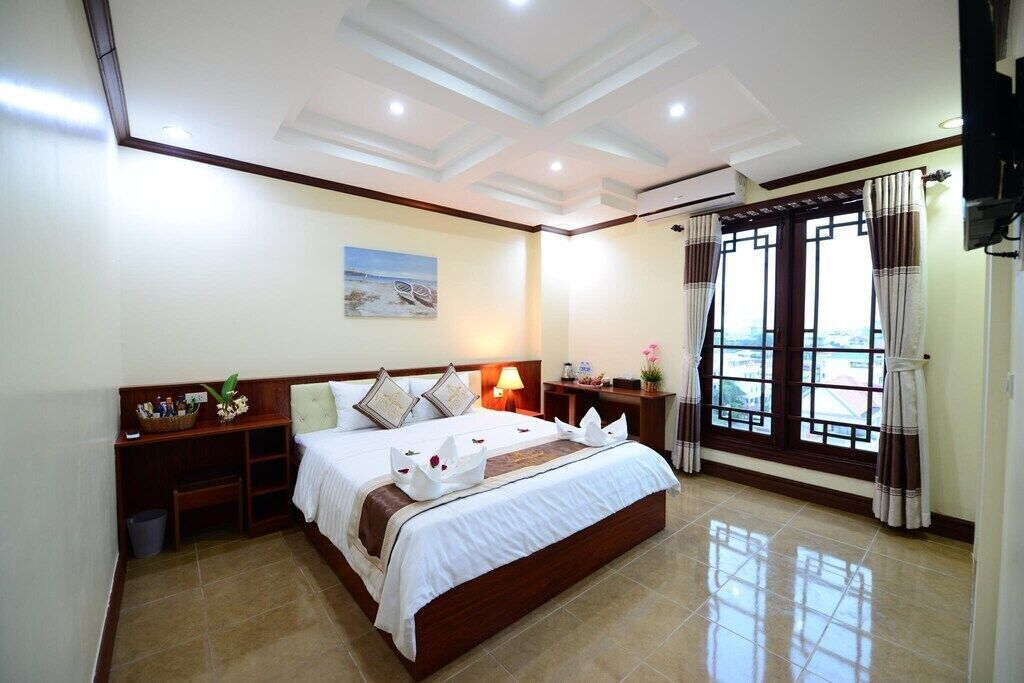 A hotel room with a large bed, a nightstand, a lamp, and a window with curtains.