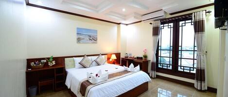 A hotel room with a large bed, a nightstand, a lamp, and a window with curtains.