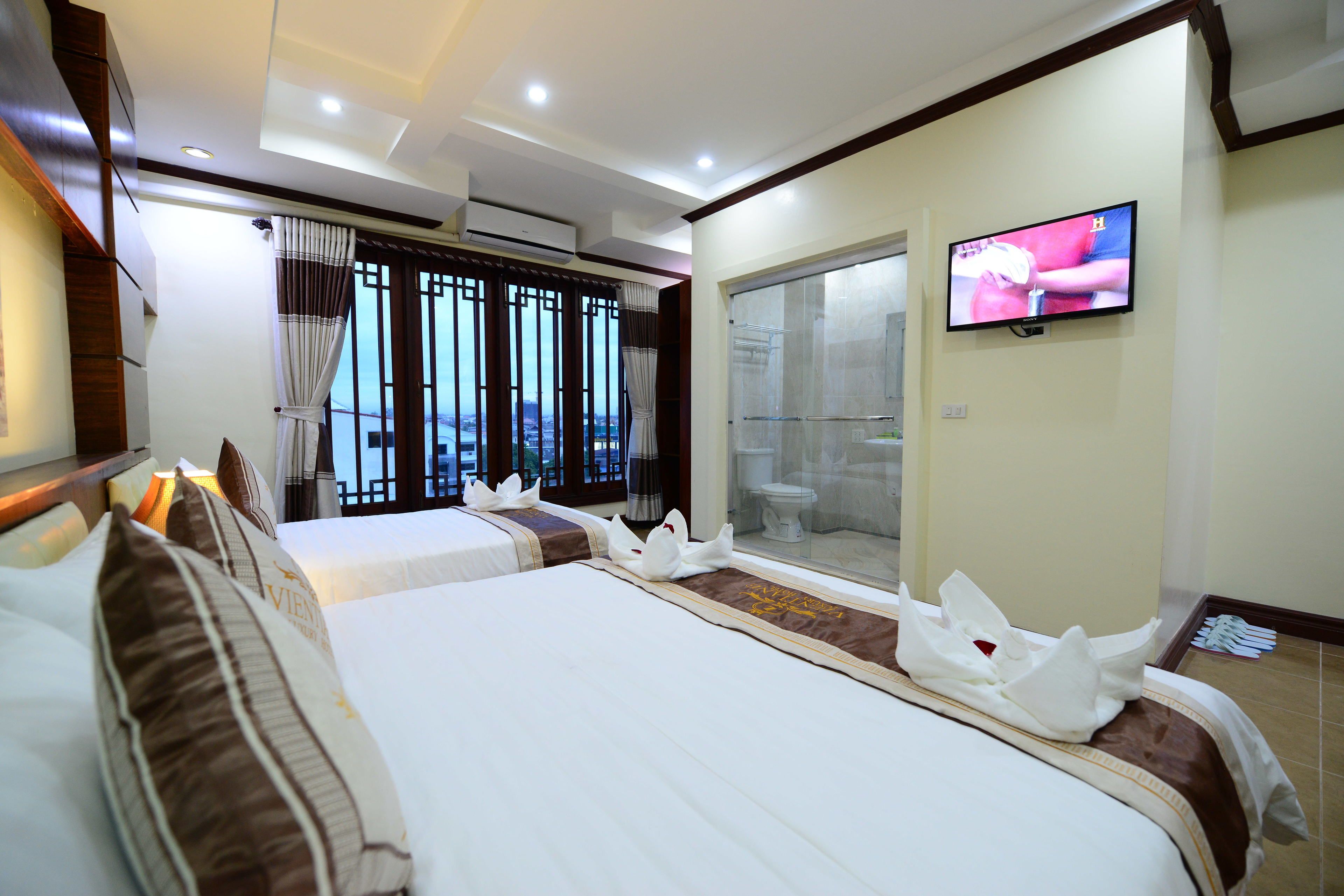 Ein Hotelzimmer mit zwei Betten, einem Fernseher und Blick auf die Stadt.