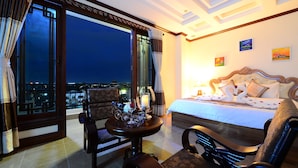 Una camera d'hotel con un letto grande, un angolo salotto con un tavolo e vista sulla città di notte.