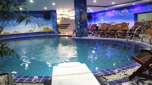 Una piscina interna con bordi piastrellati, poltroncine relax e un murale con scene subacquee.