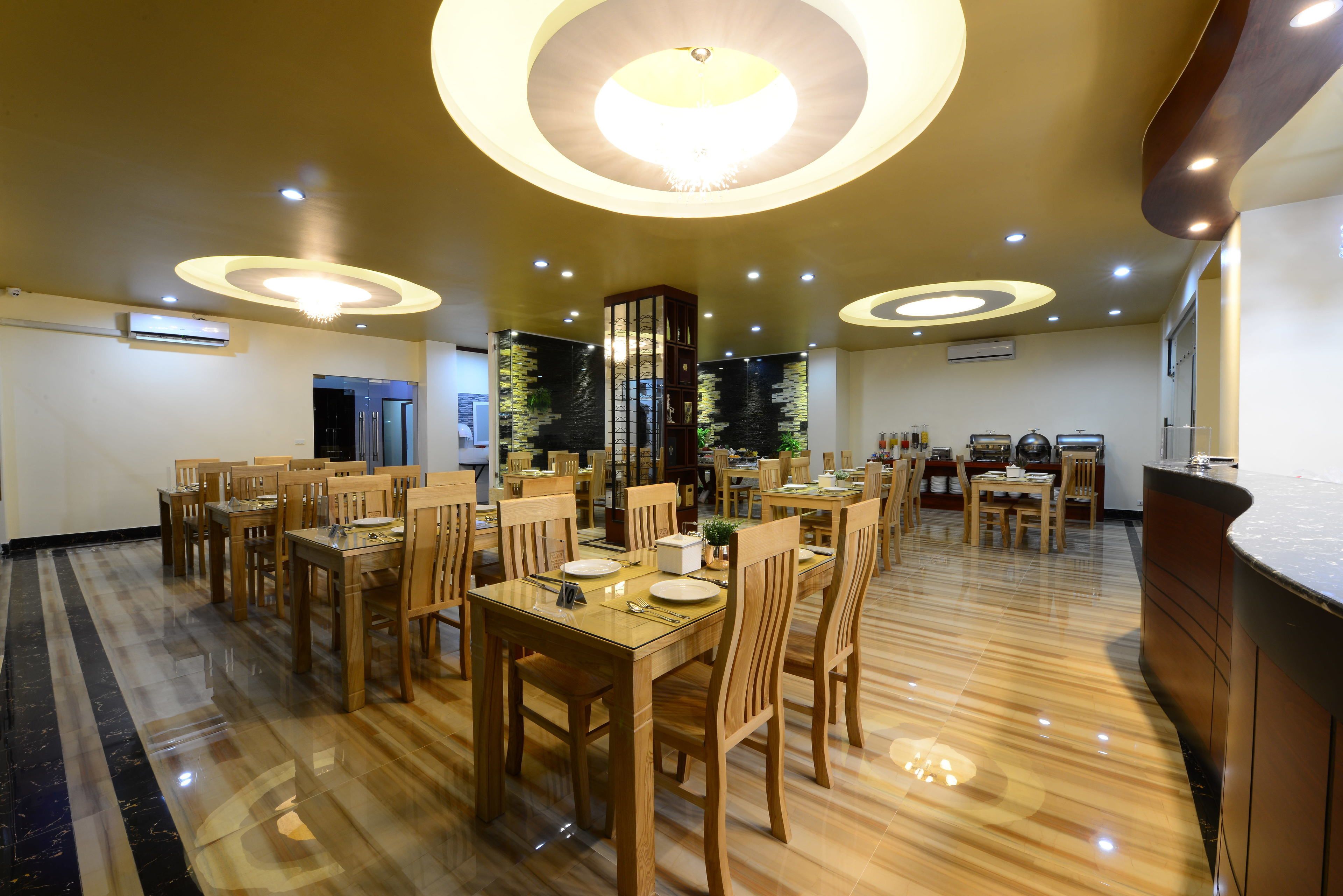 Un comedor espacioso con mesas y sillas de madera, iluminación empotrada y suelo pulido.